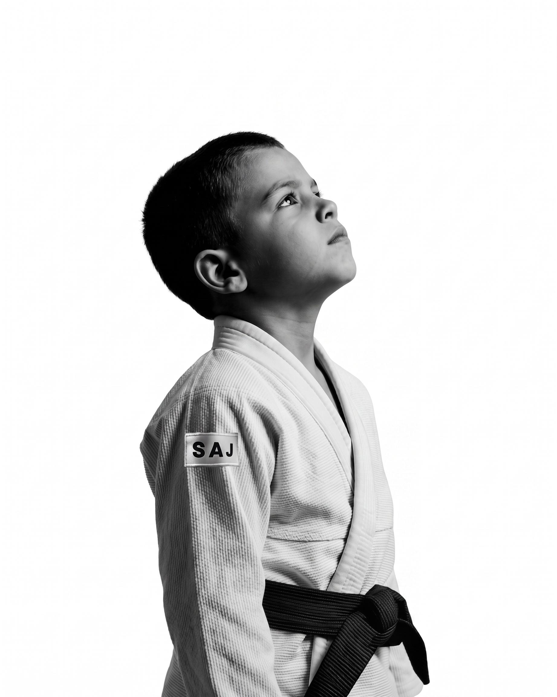 Aluno da Academia Kids de kimono branco SAJ e faixa preta, visto de perfil.